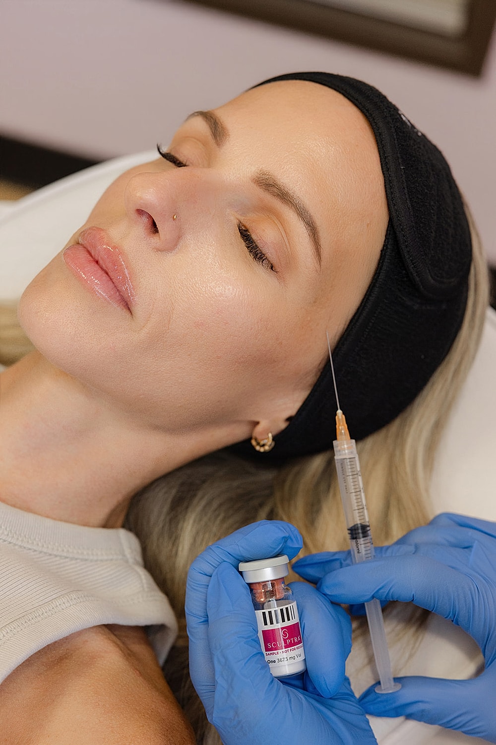 Woman receiving cosmetic treatment with syringe and vial.